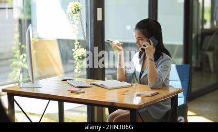 Attractive female assistant or secretary talking on the phone with her boss client, contact her supplier agent, answering phone in the office. Stock Photo