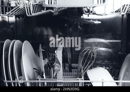 Front view of open automatic stainless steel built-in fully integrated top control dishwasher range machine with clean utensils, cutlery, glasses, dishes, plates inside in modern home kitchen Stock Photo