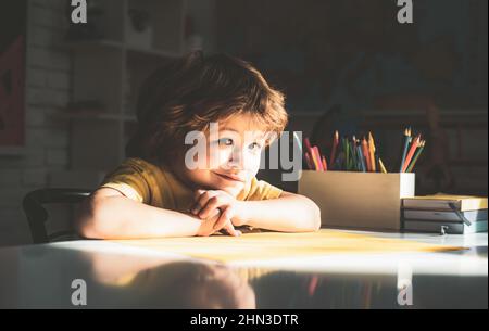 Cute pupil with funny face schooling work. Cute little preschool kid boy with teacher study in a classroom. Educational process. Stock Photo