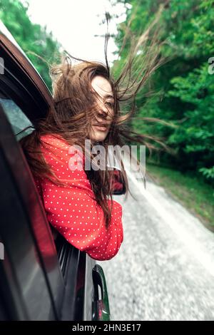 A girl in a light red airy dress, a leather jacket in a rockstyle on an empty road in a summer forest Stock Photo