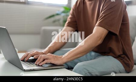 Technology Concept The man in brown T-shirt concentrating on typing something on his computer laptop. Stock Photo