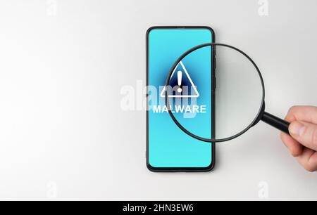Hand with magnifying glass on cell phone, an alarm sign detecting malware. Virus malware under magnifying glass, anti-virus finds malicious app. Searc Stock Photo