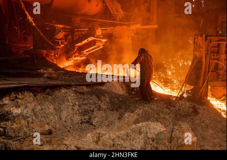 The process of releasing pig iron from a blast furnace. A man works with molten metal Stock Photo