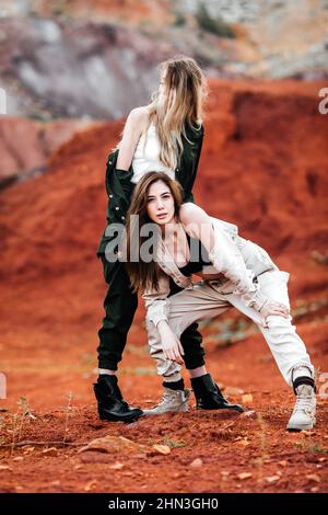 Girls in a post-apocalyptic place, a quarry with red earth and stones in work clothes Stock Photo