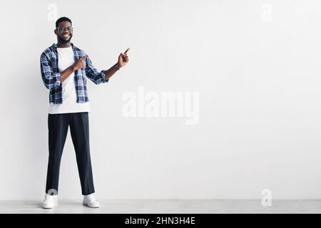 Handsome young black man pointing aside at copy space for your advertisement against white studio wall Stock Photo