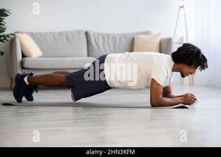 Domestic Sports. Young African American Man Doing Plank Exercise At Home Stock Photo