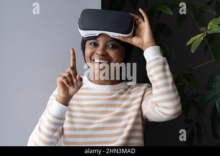 Future of VR. Happy young afro female holding virtual reality headset and looking happily at camera Stock Photo