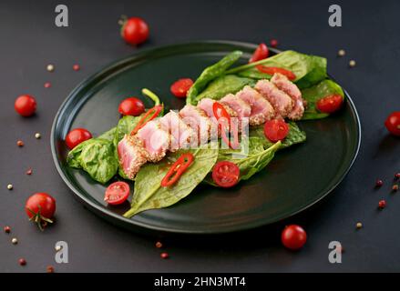 Cold appetizer of beef carpaccio with spinach and tomatoes on a black Stock Photo