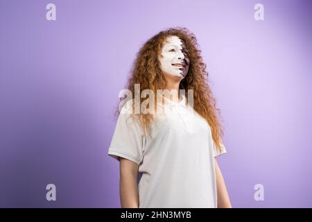 Photo of beautiful amazing redhead with curly hairstyle fan football woman with face painted in Qatar flag standing on violet background and looking Stock Photo