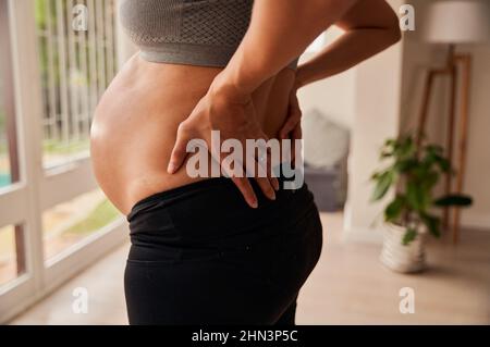Caucasian female mother to be standing in living room showing off pregnant belly  Stock Photo