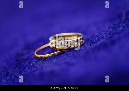 two gold shining wedding rings with diamond on dark blue background. macro photo Stock Photo