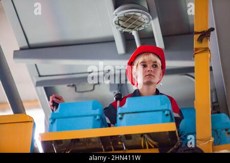 Karagandy,Kazakhstan-June 08,2012: KazBELAZ quarry trucks BELAZ service and repairing plant. Young woman crane operator in cabin. Blue switchers with Stock Photo