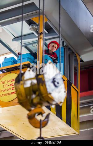 Karagandy, Kazakhstan-June 08,2012: KazBELAZ quarry trucks BELAZ service and repairing plant. Young woman crane operator in cabin. Blurred crane hook Stock Photo