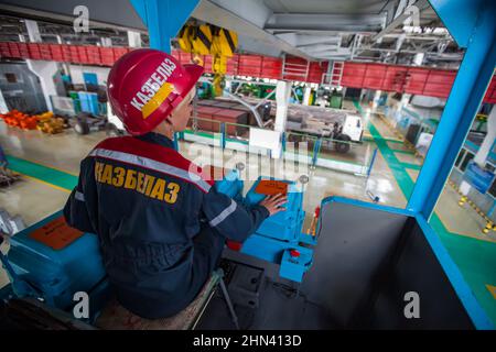 Karagandy, Kazakhstan-June 08,2012: KazBELAZ quarry trucks service and repairing plant. Young woman crane operator in cabin. logo on red helmet and wo Stock Photo