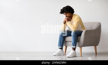 Heavy Thoughts. Portrait Of Pensive Young African American Male Sitting In Armchair Stock Photo