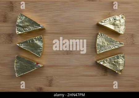 Pieces of processed cream cheese spread on wooden cutting board. Family portion of six triangles in gold foil. Minimalist background. Close-up, top view, copy space Stock Photo