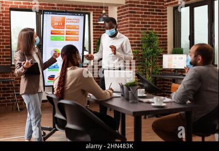 African american businessman explaining marketing strategy working at business presentation in startup company office. Businessteam with medical face mask against covid19 brainstorming project ideas Stock Photo