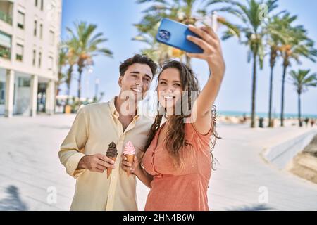 Man and woman couple eating ice cream and make selfie by the smartphone at seaside Stock Photo