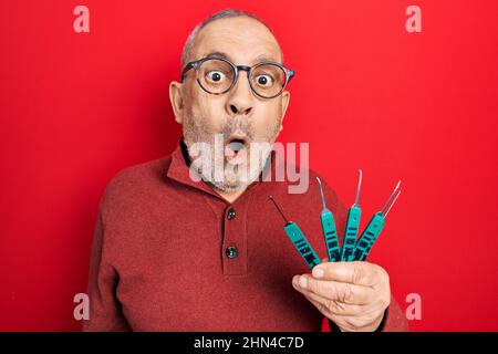 Handsome mature man holding picklock to unlock security door scared and amazed with open mouth for surprise, disbelief face Stock Photo