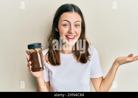 Young brunette woman holding soluble coffee celebrating achievement with happy smile and winner expression with raised hand Stock Photo