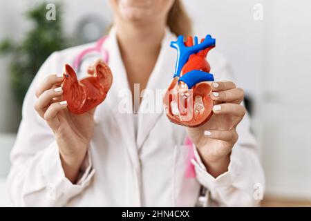 Young blonde girl wearing doctor uniform holding heart at clinic Stock Photo