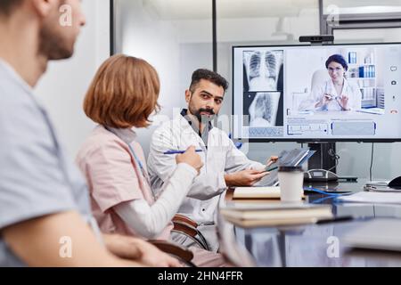 Confident mature chief physician interacting with nurse while pointing at x-ray image against female colleague on computer screen Stock Photo