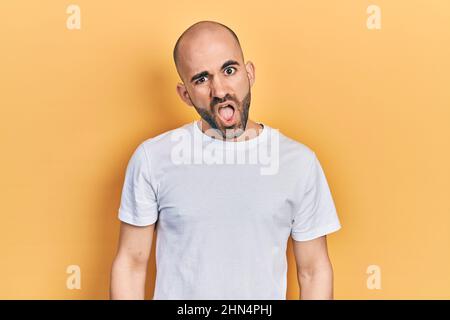 Young bald man wearing casual white t shirt in shock face, looking skeptical and sarcastic, surprised with open mouth Stock Photo
