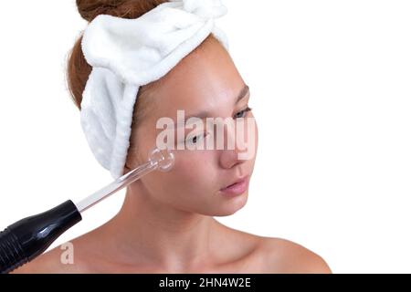 Isolated portrait of caucasian young woman without make up with band on head holding darsonval on face looking down on white background Stock Photo