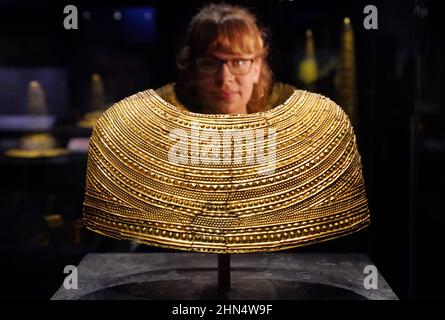 A member of staff observes a gold cape dating from 1600-1900 BC from Mold, Flintshire, Wales, during the press preview for the new The World of Stonehenge exhibition at London's British Museum. The display is the UK’s first ever major exhibition on Stonehenge and the largest British Museum exhibition of recent times, featuring over 430 objects on show from across Britain, Ireland and Europe. Picture date: Monday February 14, 2022. Stock Photo