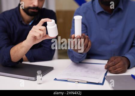 Two young intercultural male pharmacologists presenting new improved supplements or vitamins developed in chemical laboratories Stock Photo