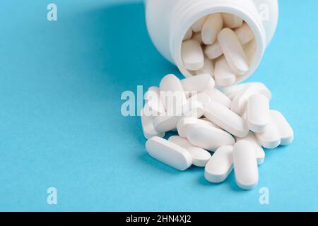 White pills with bottle on blue background with copy-space Stock Photo