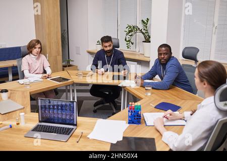 Four young contemporary experts discussing results of clinic research of new medicaments, vitamins or supplements developed in lab Stock Photo