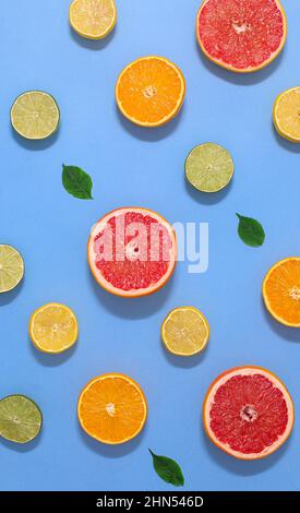 Tropic pattern with citrus sliced fruits and green leaves on vibrant cyan or blue background. Flat lay summer food Stock Photo