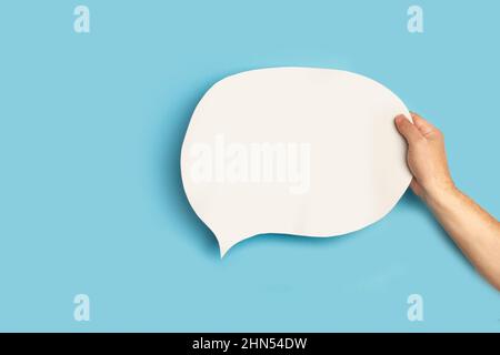 Man hand holding a blank white chat bubble on a blue background Stock Photo