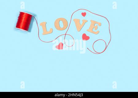 Red thread spool with love word in wooden letters on a light blue background Stock Photo