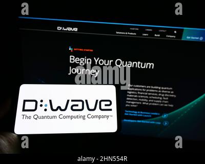 Person holding cellphone with logo of Canadian hardware company D-Wave Systems Inc. on screen in front of business webpage. Focus on phone display. Stock Photo