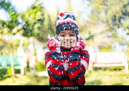 portrait of happy smiling shivering Indian girl kid standing on winter snowfall - concept of fun, joyful and freezing environment Stock Photo