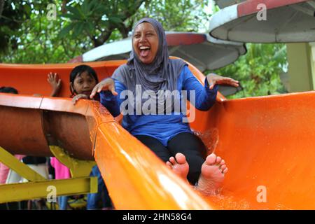 Tangerang, Indonesia - 11 19 2020: a woman in a hijab who looks happy while playing slides in a swimming area Stock Photo