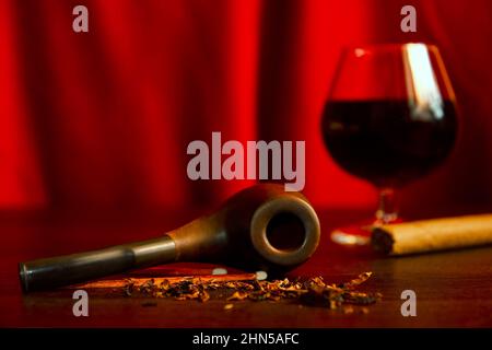 Tobacco, smoking pipe, cigar, glass with brandy on the wooden man's desk. Classic cabinet backgrounds Stock Photo