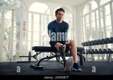 Disabled male athlete putting on his prosthetic leg in the gym Stock Photo