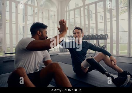 Two friends training in the gym - one with a prosthesis . Two men high fiving in the gym after a good training session Stock Photo