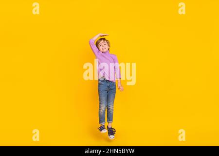 Full size photo of cheerful cute little boy jumping dreaming to become taller isolated on yellow color background Stock Photo