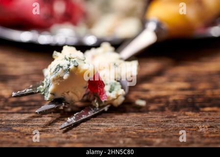 Blue cheese. Fork with blue mold cheese and pomegranate on rustic wooden table. Cheese food still life background. Stock Photo