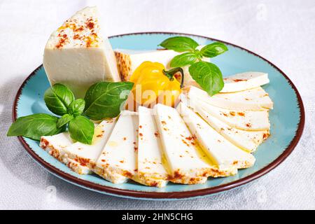 Cheese platter on white table cloth background. Plate of fresh soft cheese garnished with basil and chillies. Stock Photo