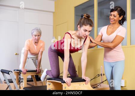 Young woman performs an exercise on a combined chair with instructor Stock Photo