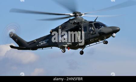 Thiene Italy, OCTOBER, 16, 2021 Modern military helicopter in dark green camouflage flying in the blue sky with the side hatch open. Agusta Westland A Stock Photo