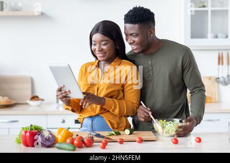 Happy Black Spouses Using Digital Tablet While Cooking Lunch In Kitchen Together Stock Photo