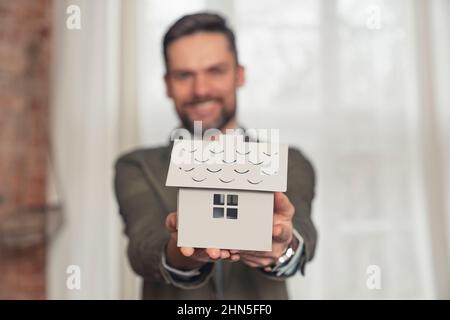 smiling businessman holding symbolic architectural house model focus on foreground. High quality photo Stock Photo