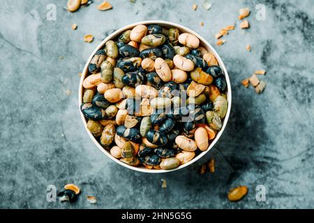 high angle view of a bowl with some roasted soya beans of different colors, served as a snack, on a veined storne surface Stock Photo