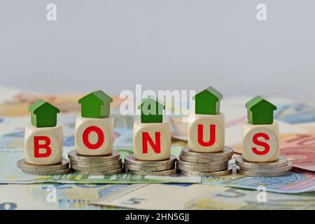 Wooden house and blocks with the word Bonus on coins and banknotes - Concept of home renovation bonus Stock Photo